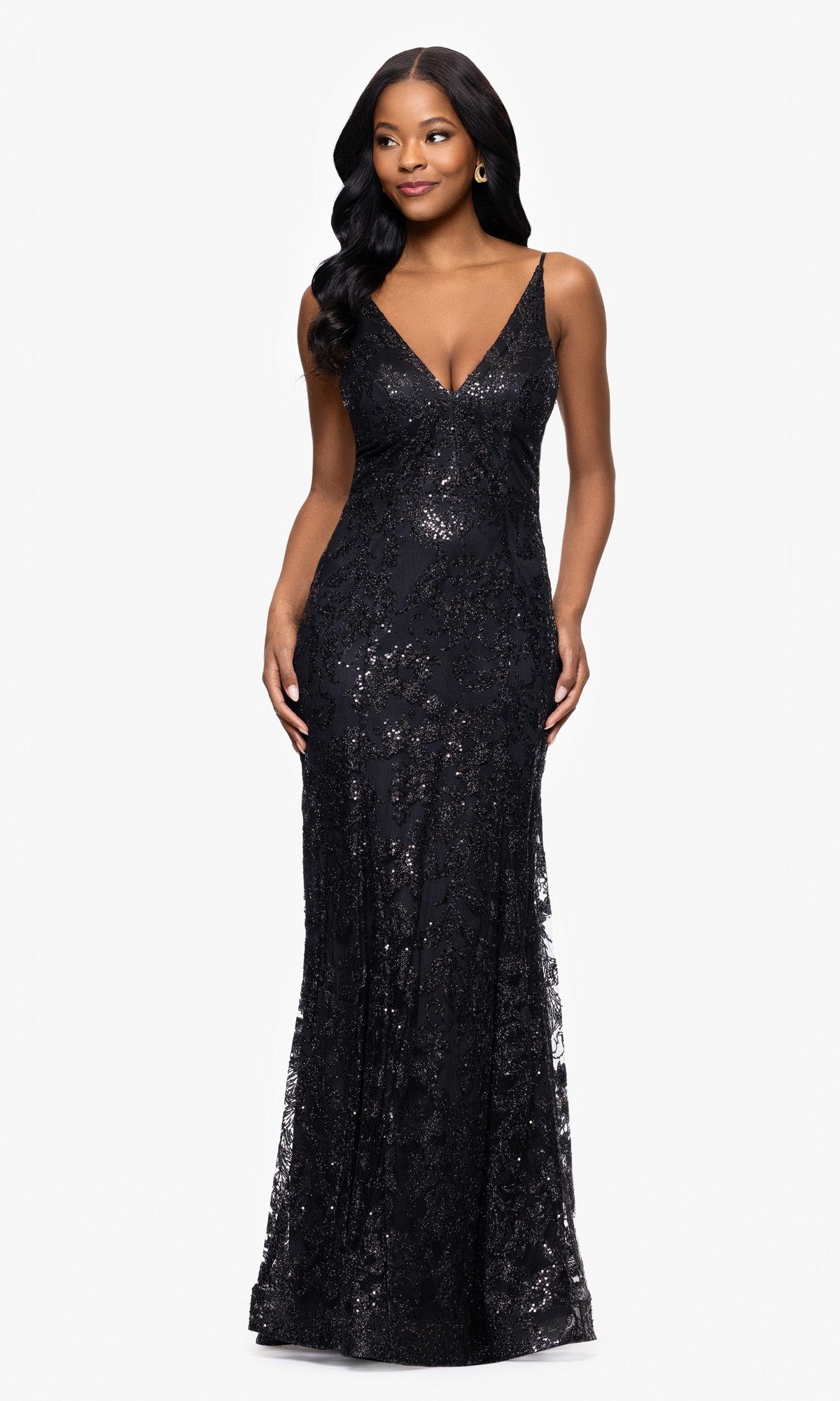 A woman stands against a plain white background wearing the Blondie Nites 4501BN Long Sequin-Print Prom Dress, featuring a deep V-neckline and strappy back.
